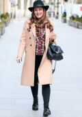 Kelly Brook a l'air super glamour avec ses cheveux ondulés, son denim serré et son manteau beige avec un chapeau fedora à Londres, au Royaume-Uni